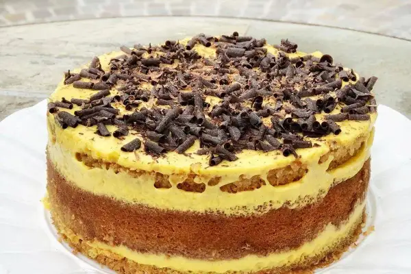 Torta pazientina a strati, con crema gialla e riccioli di cioccolato fondente in cima.