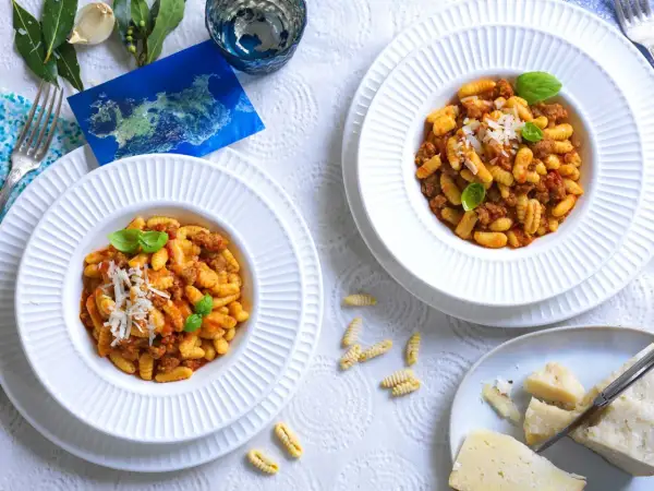 Due piatti di malloreddus alla campidanese, pasta sarda con sugo di salsiccia e pomodoro, guarniti con basilico e parmigiano.