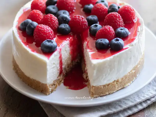 Delizioso cheesecake con mascarpone, guarnito con lamponi freschi, mirtilli e una colata di salsa rossa.