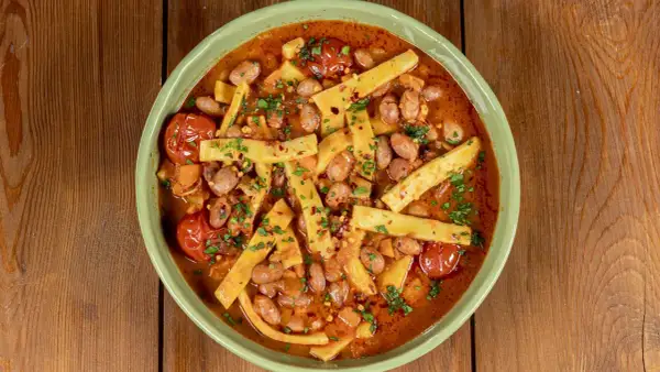 Piatto di sagne e fagioli fumante, con pomodorini e prezzemolo tritato, servito in una ciotola verde su un tavolo di legno.