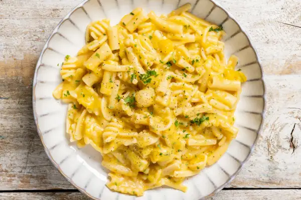 Piatto di pasta e zucca cremosa, guarnita con prezzemolo tritato e pepe nero, servita su un piatto bianco con bordo decorato.