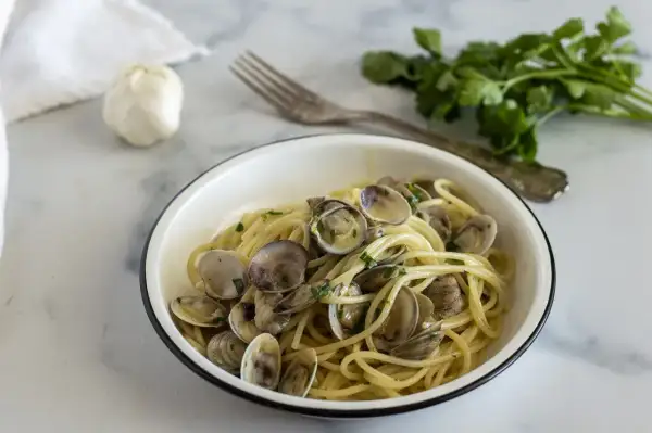 Un piatto invitante di spaghetti con le vongole, conditi con prezzemolo fresco e serviti in una ciotola bianca.