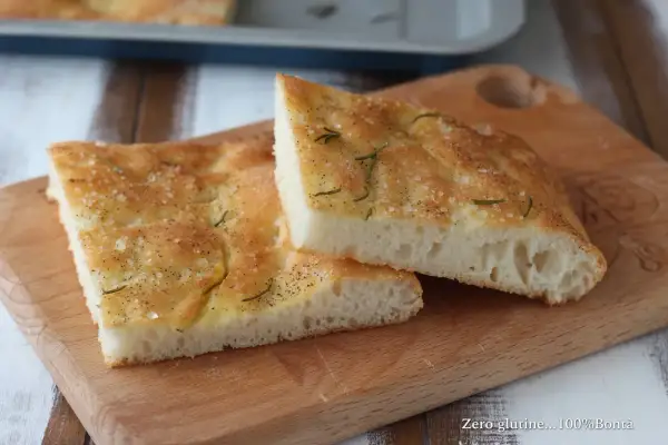 Focaccia senza glutine dorata e fragrante, condita con sale grosso e rosmarino, su un tagliere di legno.