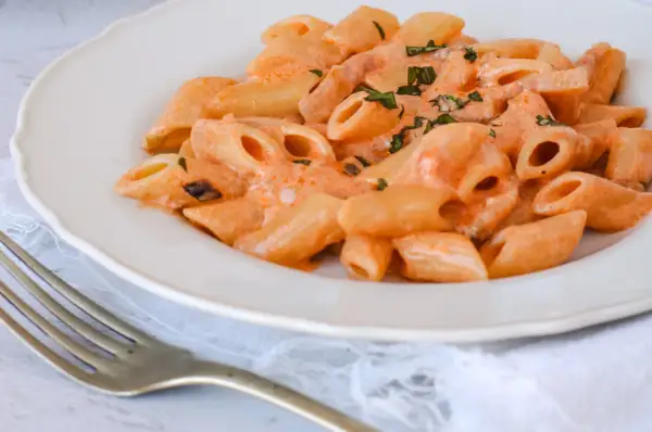 Piatto di penne alla vodka cremose, guarnite con erbe fresche, pronte per essere gustate con una forchetta.
