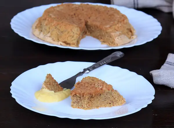 Una fetta di torta nocciole piemontese originale, soffice e dorata, servita con crema gialla.
