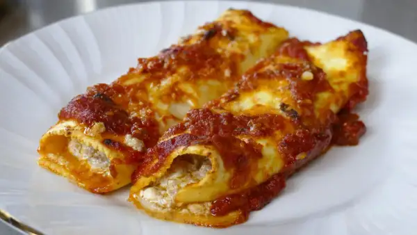 Due cannelloni di carne ripieni e ricoperti di sugo rosso, serviti su un piatto bianco.