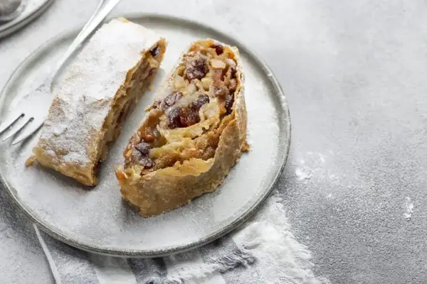 Due fette di strudel di mele su un piatto, cosparse di zucchero a velo. Un dolce invitante pronto da gustare.