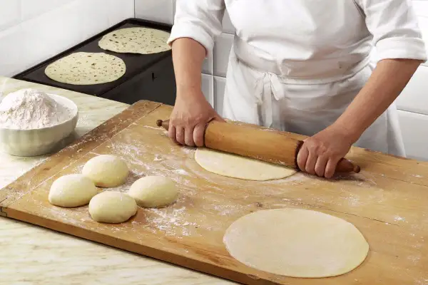 Mani esperte stendono la pasta per una piadina fatta in casa, mentre altre sono già pronte per essere cotte.