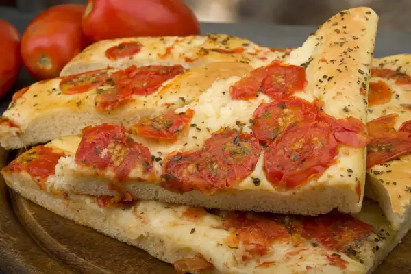 Focaccia barese soffice e dorata, condita con pomodorini freschi e origano, pronta per essere gustata.