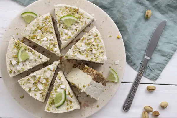 Deliziosa cheesecake vegana con lime e pistacchi, guarnita con scaglie di cocco.