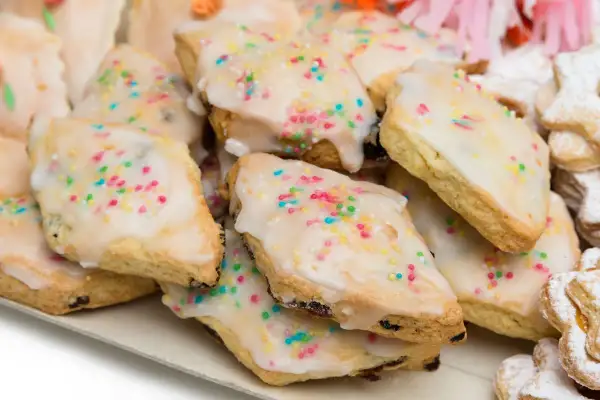 Un vassoio pieno di dolci sardi, biscotti ricoperti di glassa bianca e confettini colorati, perfetti per ogni occasione.