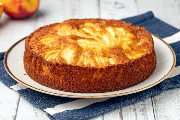 Una deliziosa torta di mele dorata, con mele a vista sulla superficie, servita su un piatto con un tovagliolo a righe blu.