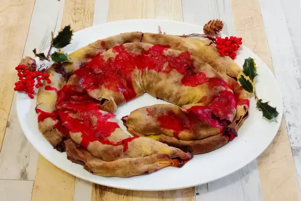 Dolce natalizio a forma di spirale, una rocciata umbra con glassa rossa e decorazioni di agrifoglio e bacche.
