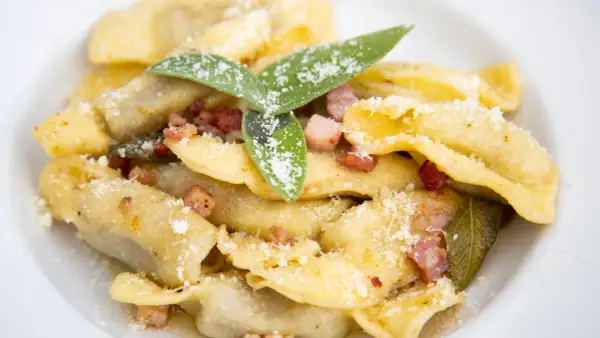 Un piatto di casoncelli alla bergamasca, ripieni e conditi con burro, salvia e pancetta croccante, spolverati di parmigiano.