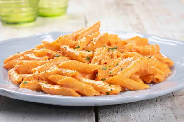 Penne cremose con salsa rosa, un classico tra le pasta ricette, guarnite con prezzemolo e parmigiano.