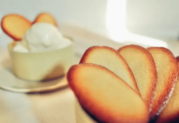 Biscotti croccanti a forma di lingue di gatto, alcuni in primo piano, altri decorano una coppa di panna montata.