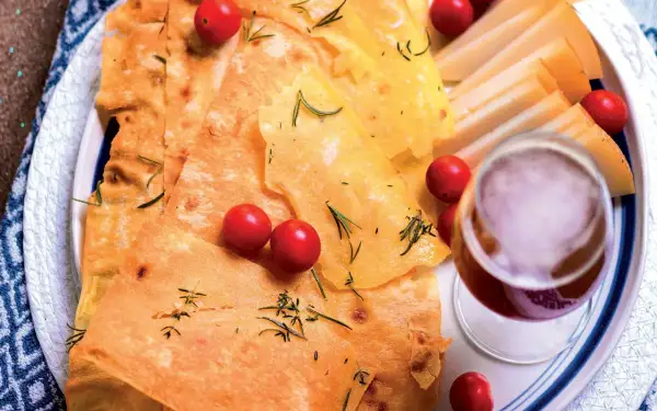 Pane guttiau croccante con pomodorini, rosmarino e fette di formaggio, accompagnato da un bicchiere di vino rosso.