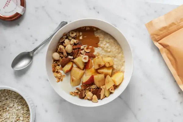 Una ciotola di avena per colazione con mele, frutta secca e burro di arachidi. Un pasto sano e gustoso.