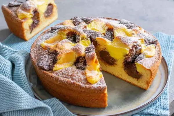 Torta nua con crema pasticcera e cacao, spolverata di zucchero a velo. Una fetta è già stata tagliata, rivelando il morbido interno.