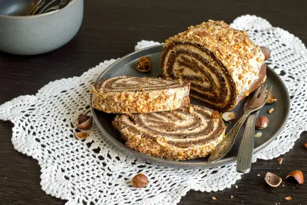 Un delizioso rotolo alla Nutella, ricoperto di granella di nocciole, servito su un piatto con due fette tagliate.