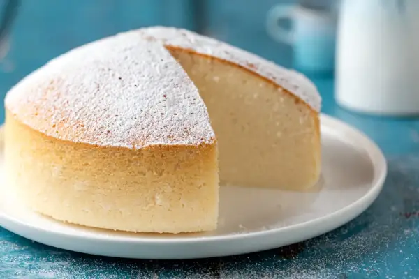 Una soffice torta nuvola, cosparsa di zucchero a velo, su un piatto bianco. La sua consistenza leggera invita a un morso goloso.