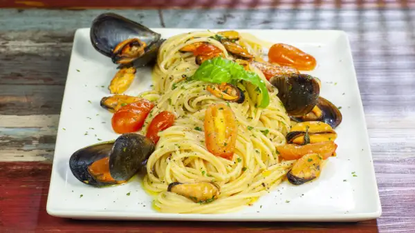 Un invitante piatto di spaghetti con le cozze e pomodorini, guarnito con basilico fresco.