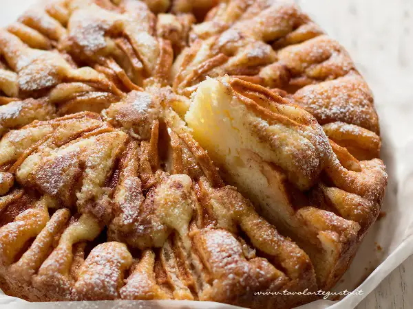 Una fetta di torta di mele morbidissima, cosparsa di zucchero a velo, con un aspetto invitante e casalingo.