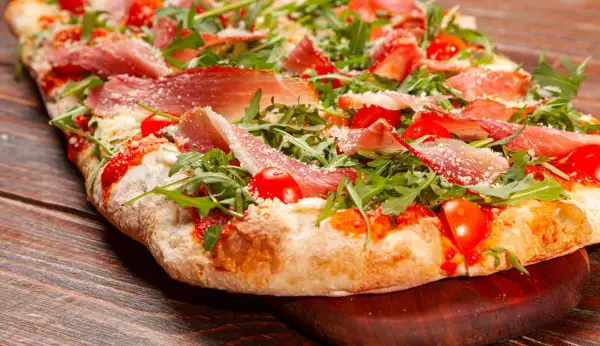 Pizza bianca con prosciutto crudo, pomodorini e rucola, cosparsa di parmigiano. Un'esplosione di sapori su un impasto soffice.