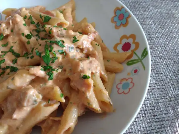 Penne al baffo cremose e gustose, condite con un sugo rosato e prezzemolo fresco, servite su un piatto decorato con fiori colorati.