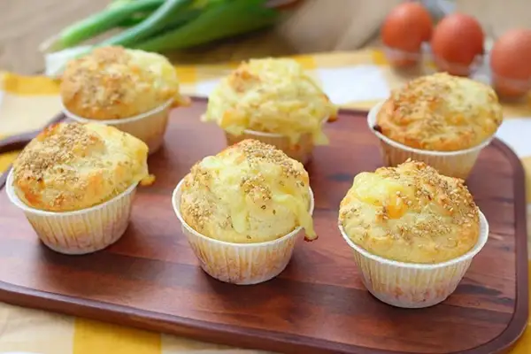 Sei muffin salati dorati, guarniti con semi di sesamo e formaggio filante, pronti per essere gustati.