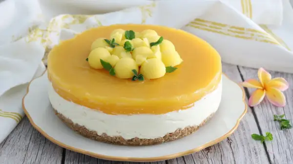 Cheesecake al mango con palline di frutta e menta fresca, su una base croccante. Un dolce estivo invitante.