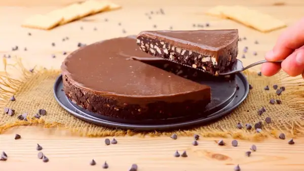 Una fetta di golosa torta fredda al cioccolato, con biscotti sbriciolati e una lucida glassa, viene sollevata da una paletta.