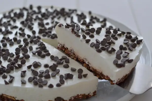 Una fetta di torta fredda allo yogurt, ricoperta di gocce di cioccolato, viene servita da una spatola.