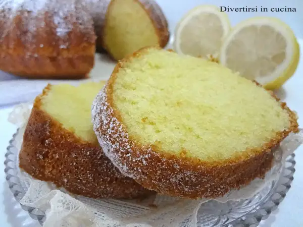 Fette di ciambellone al limone spolverate di zucchero a velo, con limoni freschi sullo sfondo.
