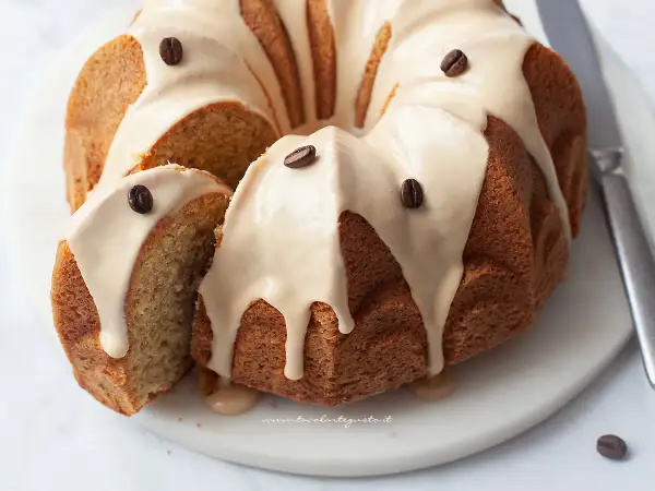 Una deliziosa torta al caffè, con glassa chiara e chicchi di caffè come decorazione. Una fetta è stata tagliata, rivelando l'interno soffice.