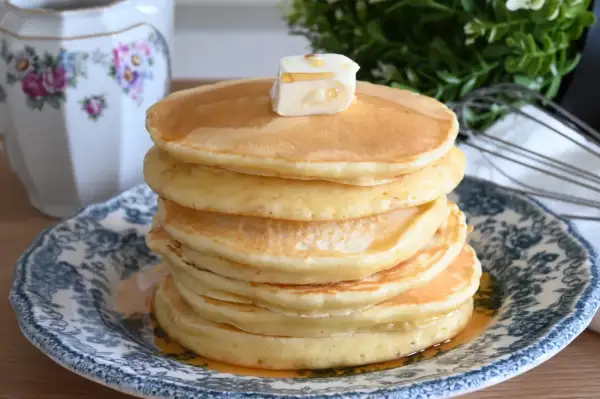 Pancake con farina di avena, una pila dorata con burro e sciroppo, serviti su un piatto decorato.