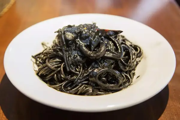 Un piatto invitante di spaghetti al nero di seppia, con anelli di calamaro e un peperoncino.