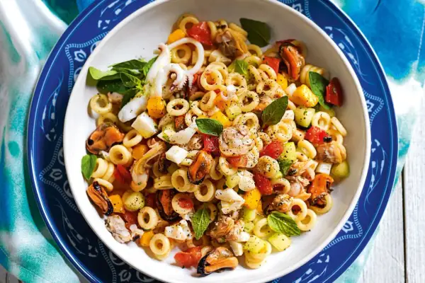 Deliziosa insalata di pasta con cozze, calamari, gamberi, pomodorini e basilico fresco. Un piatto estivo perfetto.