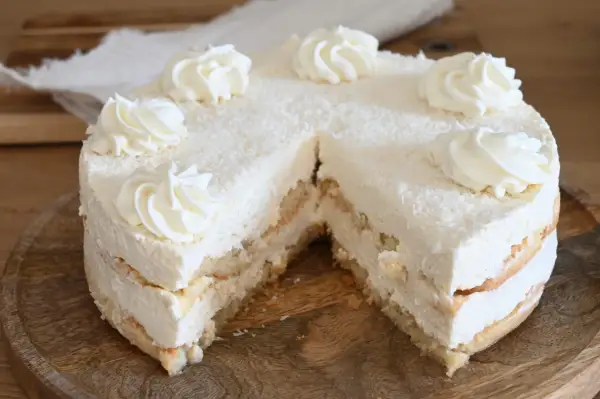 Torta soffice con strati di pan di Spagna e crema alla ricotta, ricoperta di cocco grattugiato e decorata con ciuffi di panna.