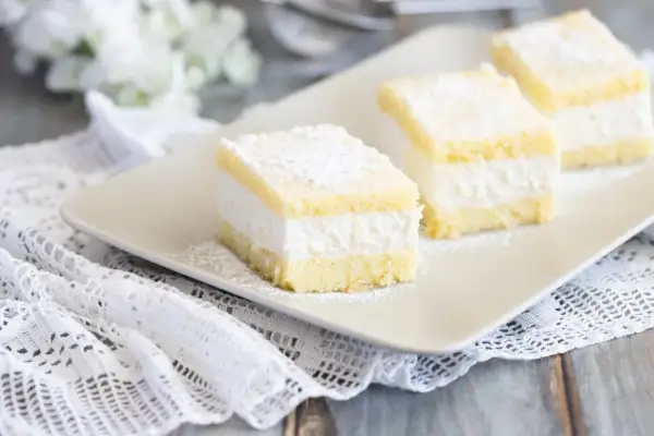 Tre soffici fette di torta Kinder Paradiso, cosparse di zucchero a velo, su un piatto bianco.