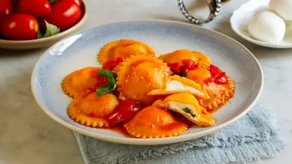 Ravioli capresi ripieni di ricotta e basilico, conditi con salsa di pomodoro fresco e guarniti con foglie di basilico.