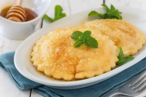Seadas ricetta: dolci fritti dorati, guarniti con miele e menta fresca, su un piatto bianco.
