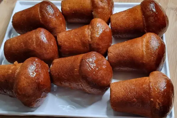 Un vassoio bianco pieno di deliziosi babà dorati, inzuppati in uno sciroppo lucido.
