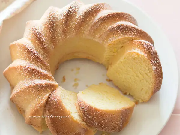 Una soffice torta di ricotta, spolverata di zucchero a velo, tagliata a fette su un piatto bianco.